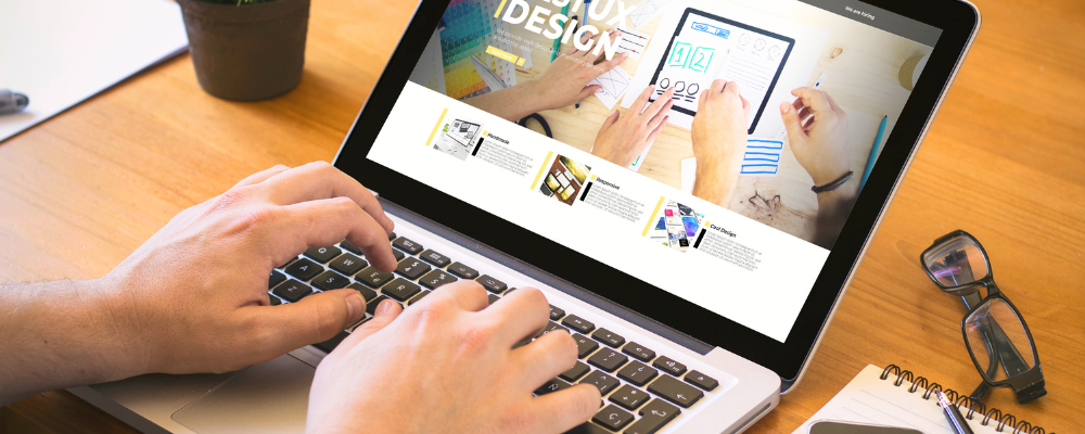 Gestaltung von Webseiten für Zahnarztpraxen und KFO-Praxen. Jemand schreibt an einem Laptop und sitzt dabei an einem Schreibtisch. Neben dem Computerbildschirm liegt eine Brille